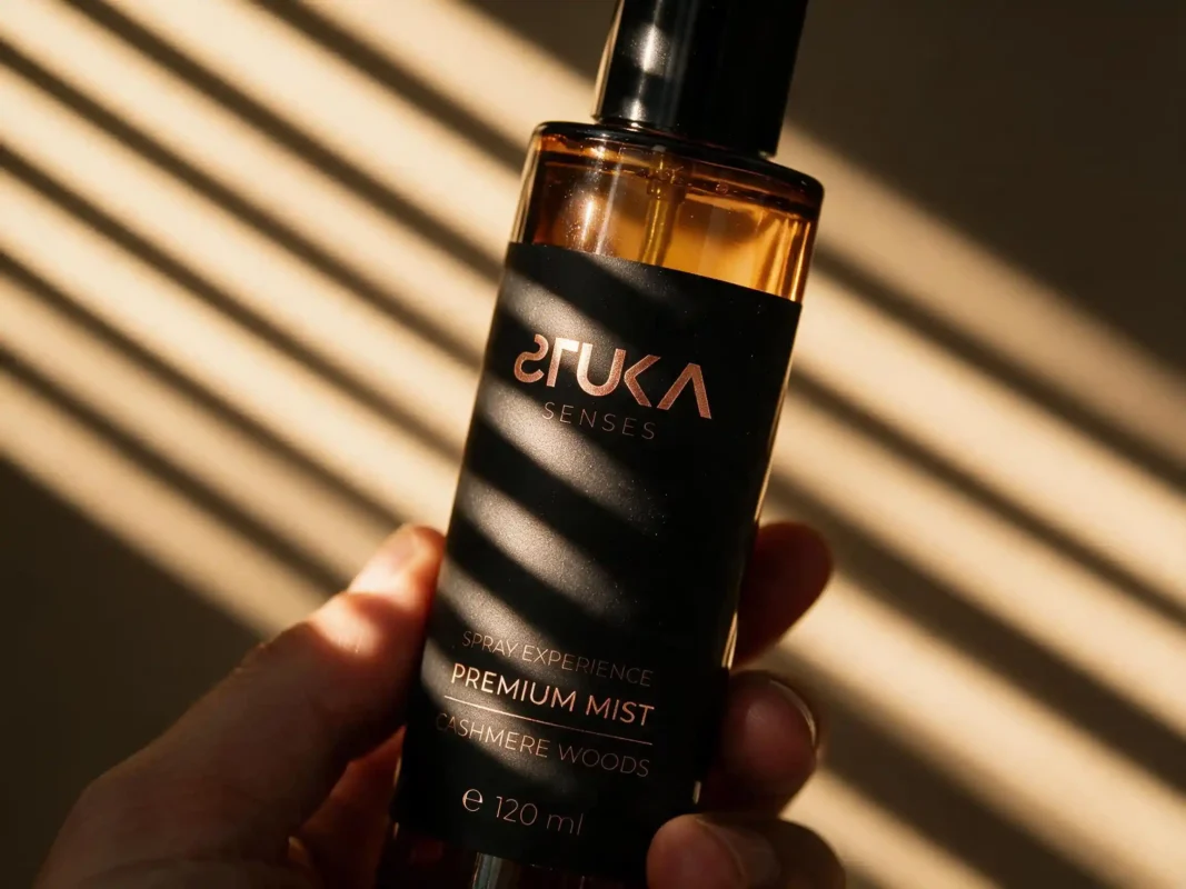 Cashmere Woods 120ml de STUKA SENSES en mano, botella negra iluminada con líneas de luz y sombra que resaltan la calidez amaderada de la fragancia